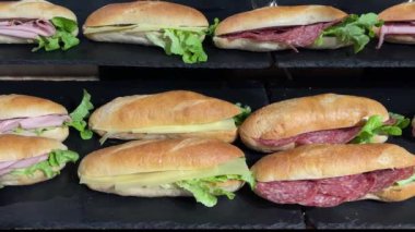 Taze mezeli sandviç çeşitleri peynir, salam, salam, salata ve salatayla birlikte siyah taş tabakta birçok sıra.