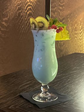 Lokanta barındaki masada meyve garnitürlü nane kokteyli. Arka planda altın duvar var. Dikey çekim.