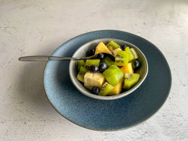 Taze tropikal meyve salata çölü mavi seramik yay üzerinde çömlek tabağı beyaz taş zemin üzerinde, renkli karışım ananas, kivi, yabanmersini, kopya alanı, yüksek açı görünüm, sağlıklı yaşam tarzı konsepti