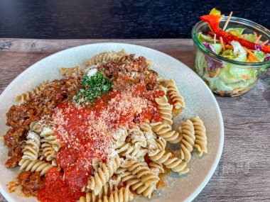 Bolonez ve domates soslu makarna, parmesan peyniri ve garnitür, cam kavanozda salata tabağı, yüksek açılı manzara, kapat.