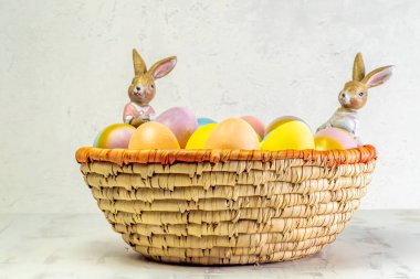 Hasır sepette tavşan figürlü Paskalya yumurtaları. Pastel renkli yumurtalar beyaz, yüksek açılı görünüm, kopyalama alanı