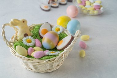 Bahar Paskalya sepeti hazırlığı. Paskalya tatlıları ve beyaz mermer taş masada pastel renkli yumurtalar. Beyaz çikolatalı tavşan, badem ezmesi ve çikolatalı badem. Hafif ve havadar, yüksek açılı görünüm, boşluğu kopyala