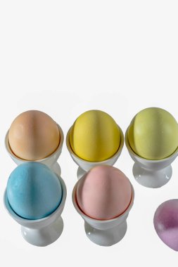 Bardakta Paskalya yumurtası. Yatay sıralar altta. Pastel renkli, beyaz arka planda izole edilmiş. yüksek açı görünümü, dikey çekim, boşluğu kopyala.