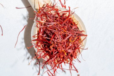 Ahşap kaşıkta kırmızı safran iplikler beyaz mermer zemin üzerine dökülüyor, güneş ışığı ve gölgelerle aydınlık ve havadar, tepeden aşağı görünüm