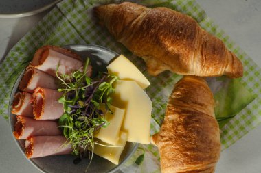 Karamsar sabah kahvaltısı. jambon, peynir ve lahanalar kasede, taze kruvasanlar yeşil örtüde, güneş ışınları ve yüksek açılı gölgeler.