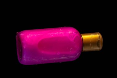 Su damlalarıyla dolu pembe kozmetik şişesi sıvıyla dolu, siyah arkaplanda yatay olarak yatıyor, boşluğu kopyala