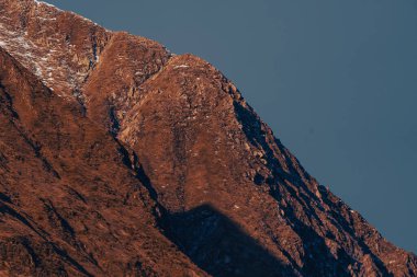 Dağ zirvesi ve tepe. dramatik kırmızı kaya uçurumu güneş ışığı altında hafif kar örtüsü, tepe ve tepenin detaylı dokusu, mavi açık gökyüzüne yakın