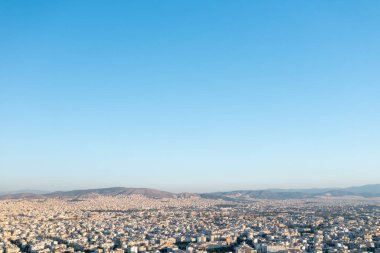 Yunanistan 'ın Atina kentinin geniş bir hava manzarası, öğle saatlerinde çekildi. Görüntü, ufka doğru uzanan binalarla kentin genişleyen şehir manzarasını gözler önüne seriyor. Çevreleyen dağlar