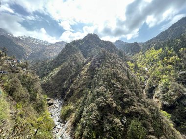 Parçalı bulutlu gökyüzünün altında yemyeşil bitki örtüsüyle kaplı dağların güzel manzarası.
