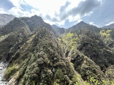 Parçalı bulutlu gökyüzünün altında yemyeşil bitki örtüsüyle kaplı dağların güzel manzarası.