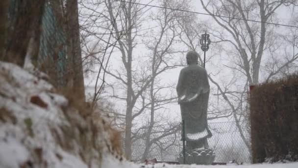 Buddhist Monk Statue Heavy Snowfall Back View Low Angle Wide — Vídeos de Stock