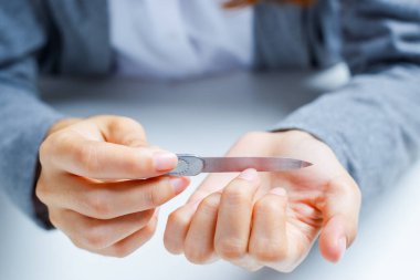Woman filing nails to remove sharpness and trim nail edges.