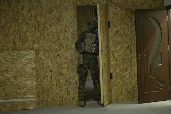 A man in a camouflage jacket stands in front of a wooden door
