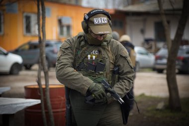 Üniformalı bir adam ekipmanını sokakta ayarlıyor, üniforması koyu yeşil.