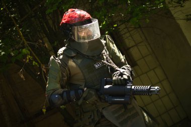 Yeşil üniformalı, kasklı, makineli tüfekli, koyu yeşil üniformalı bir adam.