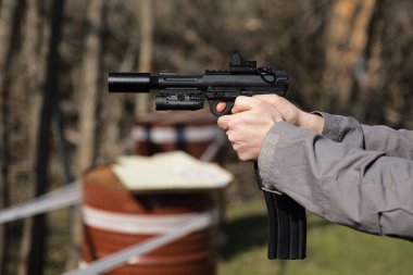 Güneşli bir günde, eller siyah bir tabancadan bir yere nişan alır.