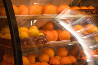 Taze limon ve portakal sepetleriyle dolu bir vitrin görüntüsü, sıcak ışık altında canlı narenciye meyveleri sergileniyor, tazelik ve sağlıkla ilgili kavramlar için mükemmel..