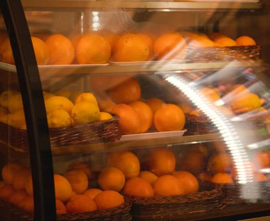 Taze limon ve portakal sepetleriyle dolu bir vitrin görüntüsü, sıcak ışık altında canlı narenciye meyveleri sergileniyor, tazelik ve sağlıkla ilgili kavramlar için mükemmel..