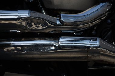 Yansıtıcı yüzeyi olan parlak krom motorsiklet egzoz borularının yakın çekimi endüstriyel tasarım ve otomotiv işçiliği sergiliyor. Cilalanmış metal, karmaşık ayrıntıları ve dokuyu vurguluyor.