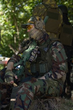 Askeri simülasyon sırasında taktik ekipman ve koruyucu gözlük takan kamuflaj üniformalı bir asker. Görüntü, modern bir savaş senaryosunun yoğunluğunu ve hazırlığını yansıtıyor..