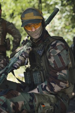 Askeri simülasyon sırasında taktik ekipman ve koruyucu gözlük takan kamuflaj üniformalı bir asker. Görüntü, modern bir savaş senaryosunun yoğunluğunu ve hazırlığını yansıtıyor..