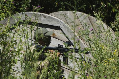 A man in tactical gear prepares his airsoft gun during an outdoor game. Wearing protective goggles, gloves, and a vest, he focuses on safety and precision in the field.
