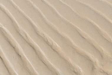 Dalgalı kahverengi kum arka planı, kumsalda kum dokusu deniz tarafından yıkanan kum yüzeyi bir desen haline geliyor..