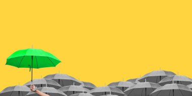 Sarı arka planda izole edilmiş gri şemsiyeler üzerinde el ele tutuşan yeşil şemsiye. Yan görüş. İş hayatında farklı bir kavram..