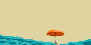 Açık sarı arka planda, diğer mavi şemsiyelerin üzerinde turuncu bir şemsiye tutuyor..