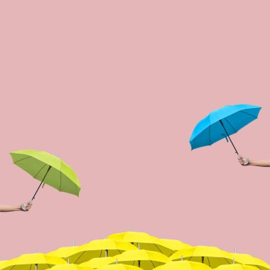 Açık pembe arka planda yeşil ve mavi şemsiyeleri diğer sarı şemsiyelerin üzerinde tutarak.