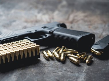 Arka planda cephanesi olan bir silah. 9 mm 'lik askeri silah. Metal masada mermi ve mermi yığını var..
