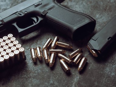 Arka planda cephanesi olan bir silah. 9 mm 'lik askeri silah. Metal masada mermi ve mermi yığını var..