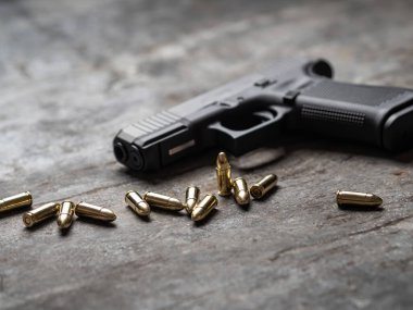 Arka planda cephanesi olan bir silah. 9 mm 'lik tabanca ve metal masada bir yığın mermi..