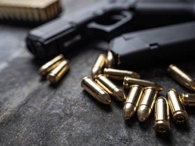 Arka planda cephanesi olan bir silah. 9 mm 'lik askeri silah. Metal masada mermi ve mermi yığını var..