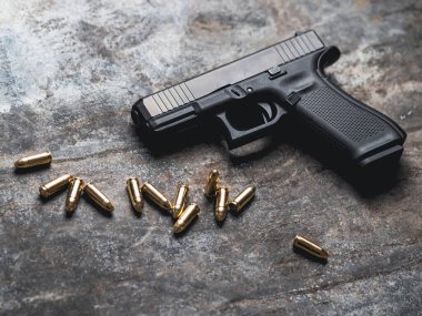 Arka planda cephanesi olan bir silah. 9 mm 'lik tabanca ve metal masada bir yığın mermi..