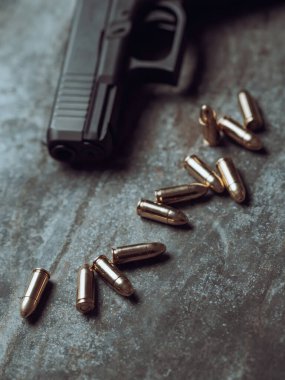 Arka planda cephanesi olan bir silah. 9 mm 'lik tabanca ve metal masada bir yığın mermi..