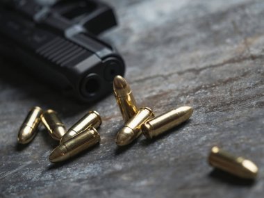 Arka planda cephanesi olan bir silah. 9 mm 'lik tabanca ve metal masada bir yığın mermi..