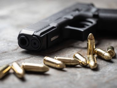 Arka planda cephanesi olan bir silah. 9 mm 'lik tabanca ve metal masada bir yığın mermi..