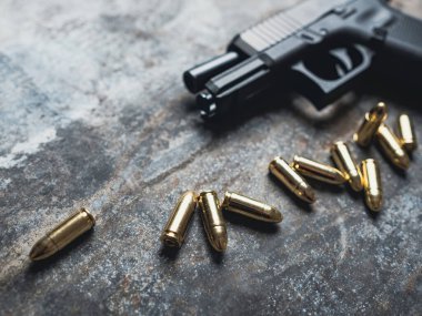 Arka planda cephanesi olan bir silah. 9 mm 'lik tabanca ve metal masada bir yığın mermi..