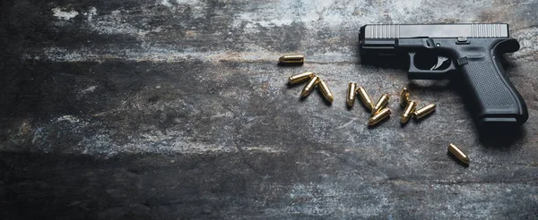 Hand gun with ammunition on dark background. 9 mm pistol military weapon and pile of bullets ammo at the metal table. Banner or wide panorama.