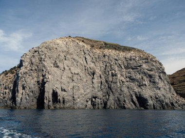 Yıpranmış deniz kenarı kaya yüzeyi dokusu ile yeşil ve mavi su parçaları. Yaşlanmış volkanik duvar yüzeyinin arka planında çatlaklar ve çizikler var. Pankart. Ischia Adası, İtalya.