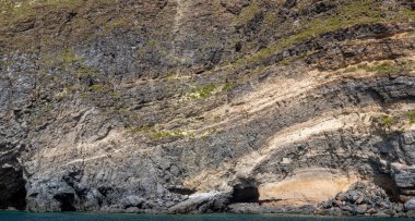 Yıpranmış deniz kenarı kaya yüzeyi dokusu ile yeşil ve mavi su parçaları. Yaşlanmış volkanik duvar yüzeyinin arka planında çatlaklar ve çizikler var. Pankart. Ischia Adası, İtalya.