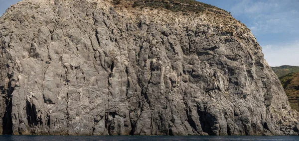 Yıpranmış deniz kenarı kaya yüzeyi dokusu ile yeşil ve mavi su parçaları. Yaşlanmış volkanik duvar yüzeyinin arka planında çatlaklar ve çizikler var. Pankart. Ischia Adası, İtalya.