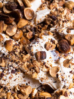 Donmuş fındık aromalı dondurma, tam çerçeve detay. Fındık parçalarıyla kaplı beyaz kremalı dondurmanın yüzey dokusunu kapat..