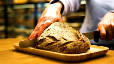 Kadın aşçı mutfak masasında taze ekmek kesiyor, yakın plan.