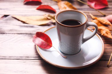 Kahverengi ahşap arka planda bir fincan kahve ve sonbahar sarı yaprakları. Sonbahar havası.