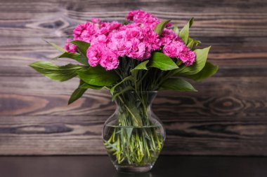 Kahverengi ahşap arka planda cam vazoda pembe karanfiller..