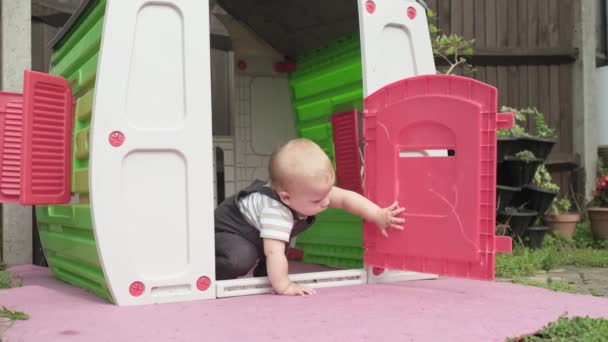 幸せな笑顔赤ちゃんの男の子の子供は プラスチック製のプレイハウスでかくれんぼをしています 小さなアクティブな子供は庭の外で一歩歩く遊び場 — ストック動画