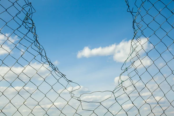 stock image Broken metal mesh fence against the blue sky. 