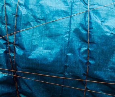 Mavi buruşmuş sentetik kumaş turuncu iplikle bağlanmış. Soyut arkaplan.